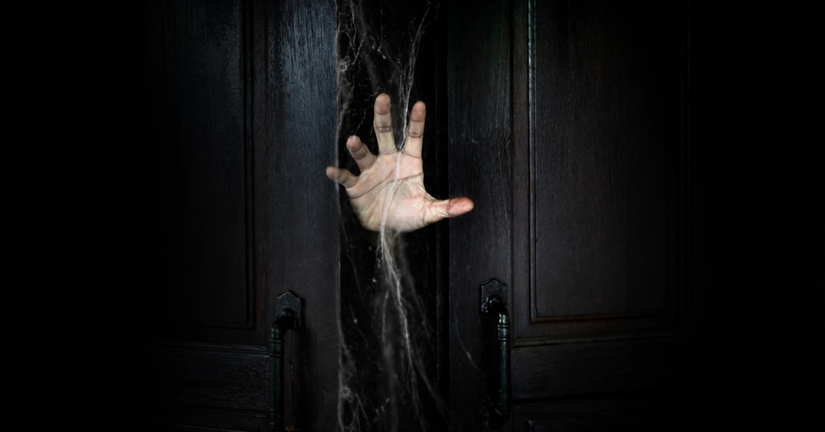 The hand of a man reaching out from a slightly open doorway. The doorway is covered in a lot of cobwebs.